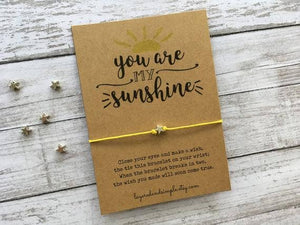 Brown card with "You are my sunshine" text, yellow string bracelet, and small star charms.