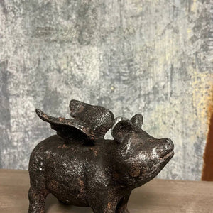 Metallic pig with wings, dark texture, against a textured gray and beige background.
