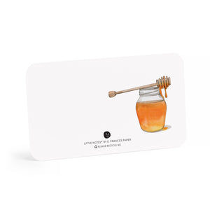A honey jar with a dipper dripping honey on a white card with rounded corners.