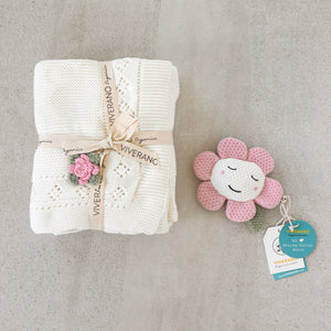 Cream knit blanket tied with ribbon and pink flower toy on gray background.