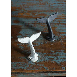 Two whale tail hooks, one white and one black, on a rustic, weathered wooden surface.