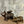 Two rustic metal pig sculptures, one with wings, on a wooden surface against a textured wall.