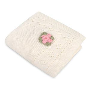 Cream knit blanket with diamond patterns and a pink and green crochet flower detail.