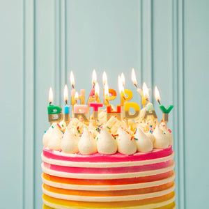 Rainbow Happy Birthday candles from Talking Tables USA arranged on a birthday cake for celebration.