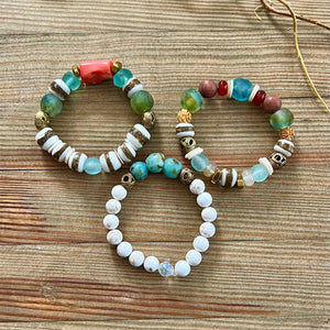 Three beaded bracelets with turquoise, white, and gold accents on a wooden surface.
