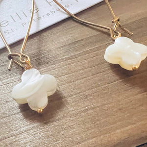 Gold earrings with white clover-shaped stones on a wooden surface.