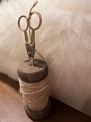 Small wooden spools with jute twine and scissors, CCOI kitchen accessory, displayed on a rustic surface.