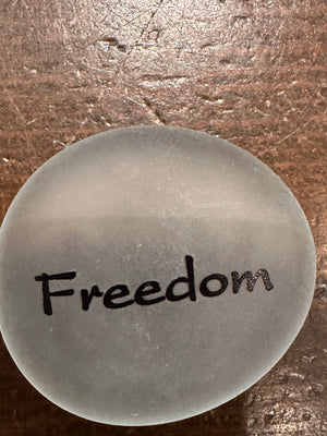 Imprinted glass word stones from SHOPGIVECOURAGE displayed in a bowl, showcasing various engraved inspirational words and symbols.