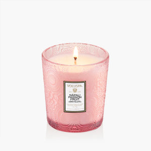 Pink glass candle with intricate patterns, labeled "Voluspa Napali Passion Fruit," lit with a flame.