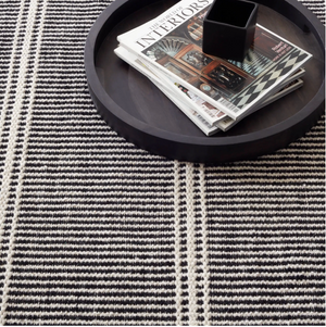 Black tray with magazines and a black cup on a striped black and white textured rug.