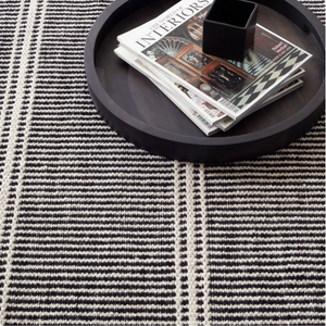 Black and white striped rug with a round tray holding magazines and a black square cup.