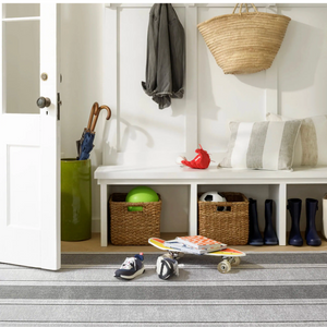 Entryway with baskets, a skateboard, shoes, and a striped rug. A coat, bag, and umbrellas are hung.