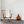 Wooden rocking chair with white blanket, amber vase, on blue-striped rug, against a white wall.