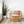 Rattan chair with floral cushion beside a tall plant in a white pot on a striped rug.