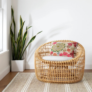 Rattan chair with floral cushion beside a tall plant in a white pot on a striped rug.