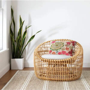 Rattan chair with floral cushion beside a tall plant in a white pot on a striped rug.