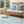 Woven sofa with blue patterned cushions, striped rug, small wooden table, and window with greenery.
