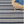 Striped navy and white rug with a round woven ottoman. Book and glasses rest on ottoman.