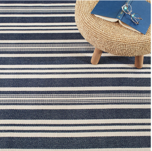 Striped navy and white rug with a round woven ottoman. Book and glasses rest on ottoman.