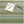 Notepad, brushes, and paint tubes on a green, blue, and beige striped surface with a glass of water.