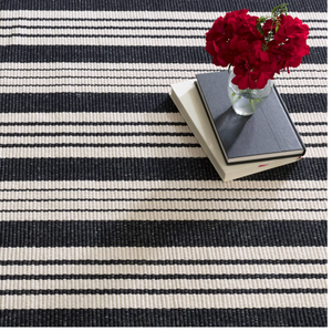 Black and white striped rug with stacked books and a vase of red flowers.