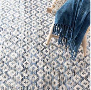 A blue and white geometric-patterned rug with a wooden chair draped in a fringed blue fabric.