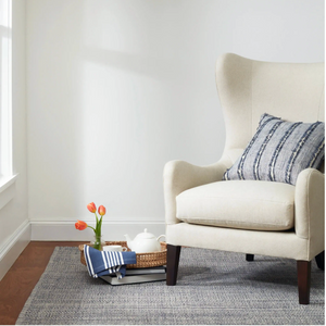 Beige armchair with a striped pillow, next to a tray with tulips and a teapot on a gray rug.