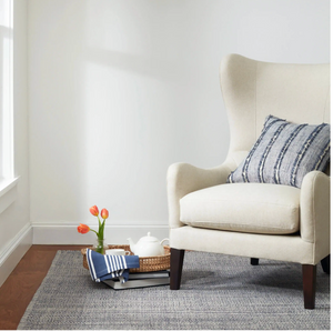 Beige armchair with a striped pillow, next to a tray with tulips and a teapot on a gray rug.