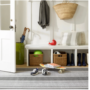 Entryway with a striped rug, skateboard, shoes, coat and bag on hooks, and baskets under a bench.