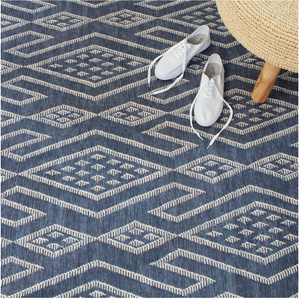 Blue geometric patterned rug with white sneakers and a woven stool on a wooden leg.