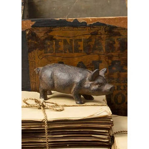 A small brown pig statue on stacked, tied papers with a vintage wooden sign in the background.