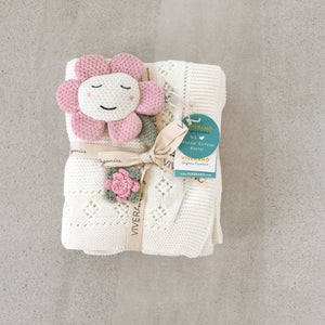 Cream knitted blanket with a pink crochet flower toy, tied with a ribbon and tag.