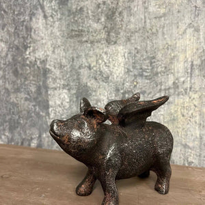 Iron pig statue with wings on a wooden surface, set against a textured gray background.