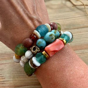 A wrist with colorful beaded bracelets, including turquoise, coral, and white stones on a wooden surface.