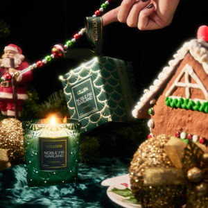 Green candle, gold accents, gingerbread house, Santa figure, and festive decorations on a dark table.