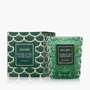 Green glass candle with intricate design beside matching patterned box, labeled "Noble Fir Garland."