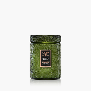 Green embossed glass candle jar with a black-and-gold label, featuring floral patterns.