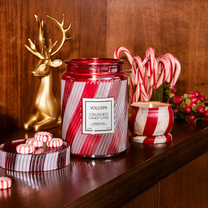 Red and white striped candle jar, golden reindeer, candy canes, and red berries on a wooden shelf.