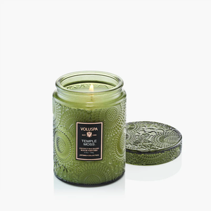 Green textured glass candle jar with lid, labeled "Temple Moss," and a soft flame burning inside.