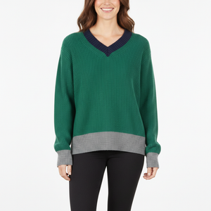 Woman in a green sweater with navy collar, gray cuffs and hem, wearing black pants on white background.