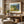 Cozy room with beige armchair, wooden table with books, and landscape painting on wood-paneled wall.