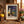 Framed painting of pumpkins, flowers, and jugs. Surroundings include books, a nest, and pink daisies.