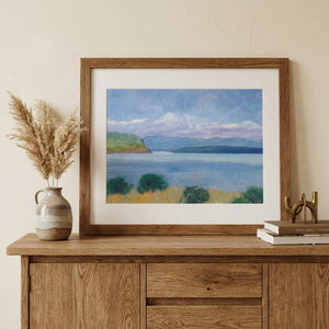 Framed landscape painting on wooden dresser with vase of pampas grass and stacked books.