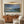 Framed seascape painting above a wooden sideboard with pottery, books, and a driftwood piece.