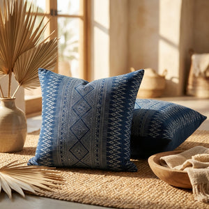 Blue cushions with intricate white tribal patterns on woven rug, surrounded by dried palm leaves.