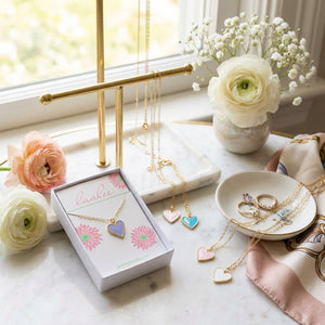 Golden necklaces with heart pendants, pastel colors, on a marble table with flowers and rings.