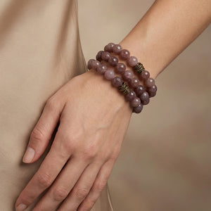 Hand with mauve beaded bracelets and bronze accents on beige background.