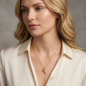 Woman with wavy blonde hair, wearing cream blouse and gold necklace with coral charm.