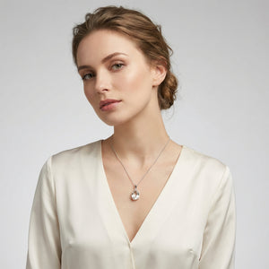 Woman with a pearl necklace, wearing a white blouse, hair in a bun, against a gray background.