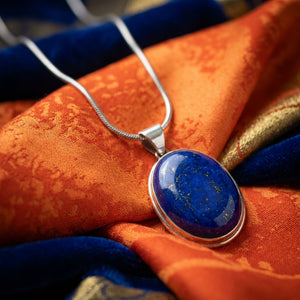 Silver necklace with blue stone pendant on vibrant orange and blue fabric.